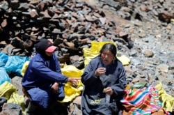 Eva Chura and another woman, who are both 'pallaqueras' known as gold pickers, smoke and drink anise while chewing coca leaves, as part of a ritual for searching for gold performed before a shift, in La Rinconada, the Andes, Peru, October 11, 2019.