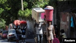 FILE - People carry their belongings along a street as they flee their homes from gang violence, in Port-au-Prince, Haiti, Oct. 26, 2024.