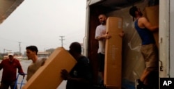 Rain-soaked furniture store workers load boxes into a truck, Sept. 15, 2018, in Fayetteville, N.C., less than a mile from the Cape Fear River, which is set to crest at 62 feet early Tuesday.