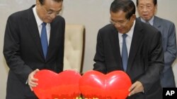 China's Premier Li Keqiang, left, pulls a symbol of China-Cambodia Heart Journey, together with his Cambodian counterpart Hun Sen, center, during a signing ceremony at Peace Palace in Phnom Penh, Cambodia, Thursday, Jan. 11, 2018. Cambodia and China on Thursday signed nearly 20 agreements worth several billion dollars to develop the impoverished Southeast Asian country's infrastructure, agriculture, and healthcare. (AP Photo/Heng Sinith)