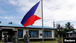 FILE - Filipino soldiers stand at attention near a Philippine flag at Thitu island in disputed South China Sea, April 21, 2017.