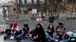 Anti-government protesters sit in front of a barbed-wire barrier on a road that leads to the Government House, during a protest in Beirut, Lebanon, Oct. 22, 2019.