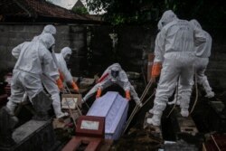 Para pegawai dinas pemakaman dengan mengenakan alat pelindung diri (APD) sedang memakamkan jenazah pasien COVID-19 di tempat pemakaman umum di Badran, Yogyakarta, 22 Juni 2021. (Foto: Hendra Nurdiyansyah/Antara Foto via Reuters)
