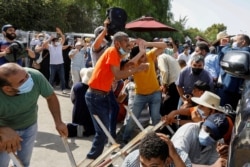 Supporters of Tunisia's biggest political party, the moderate Islamist Ennahda, take cover from stones thrown at them by supporters of President Kais Saied, outside the parliament building in Tunis, July 26, 2021.
