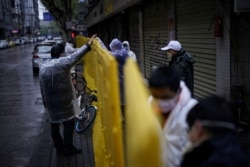 Workers wearing face masks repair barriers built up to block buildings from a street in Wuhan, Hubei province, the epicenter of China's coronavirus disease (COVID-19) outbreak.