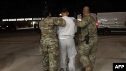 যুক্তরাষ্ট্রের প্রতিরক্ষা বিভাগের সরবরাহ করা ভিডিও-র স্ক্রিনশটে গুয়ান্তানামো বে-তে আগত আটক অভিবাসীদের প্রথম বিমান থেকে নামানো হচ্ছে, ৪ ফেব্রুয়ারি, ২০২৫।  