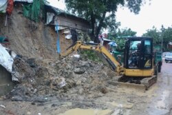 Rohingya refugees and others look on as machinery is used to remove debris after a landslide triggered by heavy rains in a camp at Ukhiya in Cox's Bazar district, Bangladesh, Tuesday, July 27, 2021