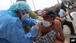 FILE - Eighty five-year-old Crisologo Enriquez holds steady as he receives a influenza vaccine during a vaccination campaign and COVID-19 testing operation in the Villa El Salvador neighborhood of Lima, Peru, June 26, 2020.