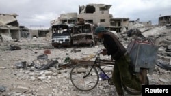 A man walks with his bicycle at a damaged site in the besieged town of Douma, in eastern Ghouta, near Damascus, Syria, March 30, 2018.