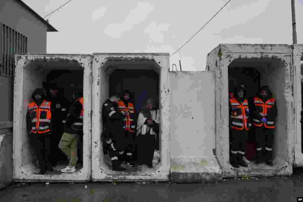 Paramedics take cover from the rain while Palestinians cross from the Israeli military Qalandia checkpoint near the West Bank city of Ramallah to Jerusalem, to participate in the Friday prayers at the Al-Aqsa Mosque during the Muslim holy month of Ramadan.