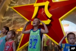 A Chinese child salutes with both hands in front of the emblem of the People's Liberation Army or PLA during an exhibition to mark the 90th anniversary of the founding of the PLA at the military museum in Beijing, China, Aug. 1, 2017.