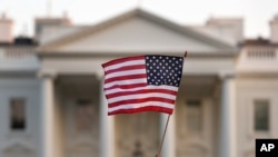 FILE - A flag is waved outside the White House, in Washington, Sept. 5, 2017. The Trump administration is extending a ban on green cards issued outside the United States until the end of 2020 and adding many temporary work visas to the freeze.
