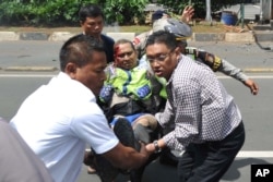 People carry an injured police officer near the site where an explosion went off at a police post, rear, in Jakarta, Indonesia, Jan. 14, 2016.