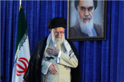 Iranian Supreme Leader Ayatollah Ali Khamenei gestures to a crowd at a June 4, 2019 ceremony in Tehran marking the 30th anniversary of the death of his predecessor, Ayatollah Ruhollah Khomeini, whose portrait appears behind him.