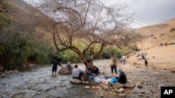 FILE - Palestinians sit under a tree in a spring near al-Auja village of the Jordan Valley, in the West Bank, Feb. 25, 2023.