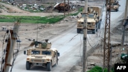 Vehicles belonging to the US-led coalition drive down a street in the front line Syrian village of Baghuz, Feb. 17, 2019. 