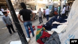 Syrians stand next to the bodies of those killed in a reported bomb barrel attack by the Syrian airforce on the eastern Shaar neighbourhood of the northern Syrian city of Aleppo, May 30, 2015. 