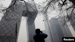 FILE - A man uses his phone while standing near the China Central Television (CCTV) building in Beijing, China, March 5, 2021. 