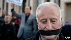 FILE - A demonstrator with his mouth covered stands outside the Istanbul courthouse, where Turkish opposition Cumhuriyet daily's editor-in-chief Can Dundar and Ankara bureau chief Erdem Gul attend their trial, April 1, 2016. 