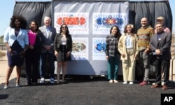 In this image provided by the U.S. Postal Service, USPS officials and artists who contributed to new skateboarding themed stamps pose in front of a display of the "Art of the Skateboard" Forever stamps in Phoenix, Friday, March 24, 2023. (Rod Spurgeon/U.S. Postal Service via AP)