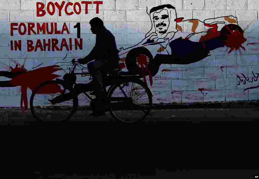 Seorang pria mengendarai sepeda melewati grafiti di dinding yang mendesak boikot kejuaraan Grand Prix Formula Satu tanggal April 21 di di kota Bar Bar, Bahrain. Grafiti ini bergambar Putra Mahkota Bahrain, Salman Al Khalifa mengendarai sebuah mobil balap.