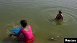 FILE - A woman washes clothes as her daughter bathes in the Yamuna River on a hot day in New Delhi, India, April 24, 2017. 