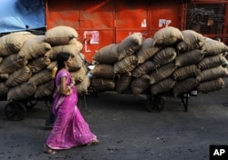 Hindistonlik ayol Nyu-Dehlidagi bozorda oziq-ovqat ortilgan qoplar yonidan o'tmoqda. 9-iyun, 2011-yil.