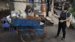 A woman buys food from a street stall vendor - with a ‘Covid safe’ plastic shield in Bangkok. (Vijitra Duangdee/VOA)