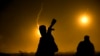 FILE - A U.S.-backed Syrian Democratic Forces fighter watches illumination rounds light up Baghuz, Syria, as the last pocket of Islamic State militants is attacked on March 12, 2019. 
