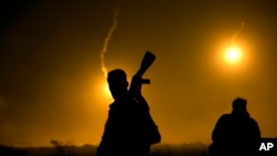 FILE - A U.S.-backed Syrian Democratic Forces fighter watches illumination rounds light up Baghuz, Syria, as the last pocket of Islamic State militants is attacked on March 12, 2019. 