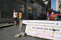 Residents wearing face masks walk past a checkpoint along a street in Manila, Philippines, March 27, 2020, after the government imposed an enhanced quarantine as a preventive measure against the spread of the coronavirus.