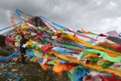 FILE - A Tibetan man ties prayer flags to a shrine at the foot of the Amnye Machen mountains on the eastern edge of the Tibetan Plateau in northwestern China's Qinghai Province, Aug. 20, 2018.
