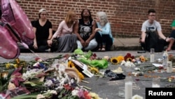 Women sit by an impromptu memorial of flowers commemorating the victims at the scene of the car attack on a group of counterprotesters during the "Unite the Right" rally as people continue to react to the weekend violence in Charlottesville, Virginia, Aug. 14,