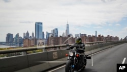 Ashley Zeolla rides her motorcycle over the Williamsburg Bridge on a delivery run of personal protective equipment to a doctors office with Masks for Docs as the lower Manhattan skyline looms in the distance, May 3, 2020, in New York. 