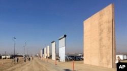 FILE - People look at prototypes of a border wall, Oct. 26, 2017, in San Diego, California. Contractors have completed eight prototypes of President Donald Trump's proposed border wall with Mexico, triggering a period of rigorous testing.
