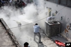 A policeman tries to disperse hundreds of migrants by spraying them with a fire extinguisher during a registration procedure that was taking place at the stadium of Kos town, on the southeastern island of Kos, Greece, Aug. 11, 2015.