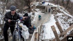 FILE - Local residents walk across a bridge damaged during fighting between Ukrainian government forces and Russia-backed rebels in Stanytsia Luhanska, Luhansk region, eastern Ukraine, Jan. 16, 2016.