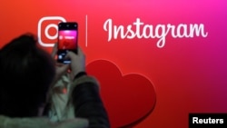 FILE - A visitor takes a picture of the Instagram app logo in Paris, France, Feb. 7, 2018. 