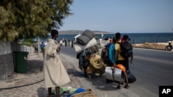 Migrants carrying their belongings, walk on a road near Mytilene town, on the northeastern island of Lesbos, Greece, Sept. 14, 2020. 
