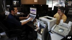 FILE - An internet cafe manager works on his computer as a man talks on his cellphone, in Tehran, Iran, July 25, 2019.