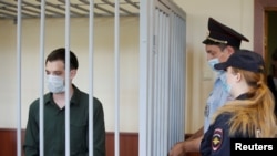 FILE - Former U.S. Marine Trevor Reed, who was detained in 2019 and accused of assaulting two police officers, stands inside a defendant's cage during a court hearing in Moscow, Russia, July 30, 2020. 