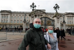 A couple wear face masks as they visit Buckingham Palace in London, Saturday, March 14, 2020.