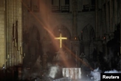 Smoke rises around the alter in front of the cross inside the Notre Dame Cathedral as a fire continues to burn in Paris, France, April 16, 2019.
