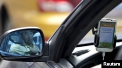FILE - A taxi driver is reflected in a side mirror as he uses the Didi Chuxing car-hailing application in Beijing, China, Sept. 22, 2015. 