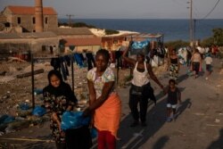 Refugees and migrants from the destroyed Moria make their way near a field as they are sheltered near a new temporary camp, on the island of Lesbos, Greece, Sept. 15, 2020.