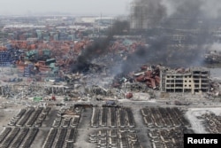 FILE - Smoke rises among shipping containers next to damaged vehicles as firefighters try to put out a fire after explosions on Wednesday night, at Binhai new district in Tianjin, China, Aug. 14, 2015.
