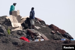 FILE - Migrants gather cardboard to build makeshift shelters near the former "Jungle" in Calais, France, June 1, 2017.