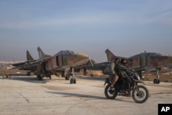 Syrian opposition fighters ride on a motorcycle past Syrian army planes at the Al-Nayrab military airport after they took control of the facility in the outskirts of Aleppo, Dec. 2, 2024.
