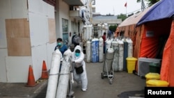 A medical worker pulls oxygen cylinders near temporary tents erected outside the emergency ward for accommodating the lack of beds at a government-run hospital in Bekasi, on the outskirts of Jakarta, Indonesia, July 15, 2021. 