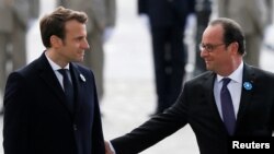 Outgoing French President Francois Hollande (R) reaches out to touch President-elect Emmanuel Macron, as they attend a ceremony to mark the end of World War II at the Tomb of the Unknown Soldier at the Arc de Triomphe in Paris, May 8, 2017. 